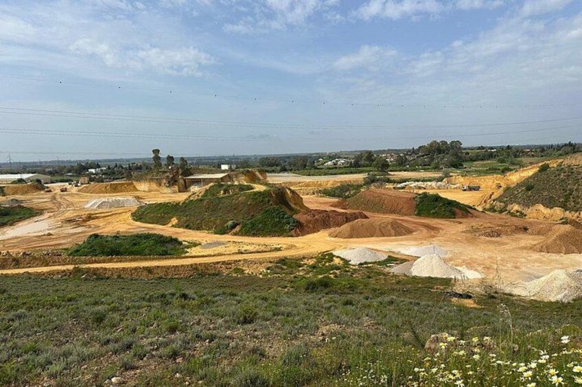 A quarry with piles of earth and construction materials, surrounded by greenery and a clear sky. 2