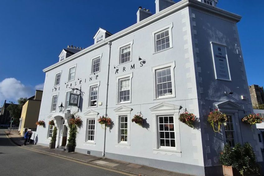 A white building with the sign 'The First Arms' and flower baskets on the windows. 4