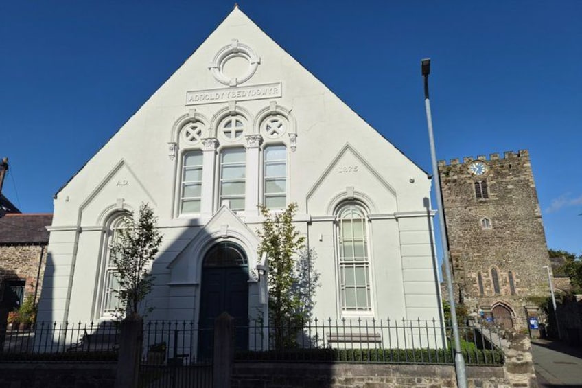 A white church with a clock tower and a stone building with arched windows. 5