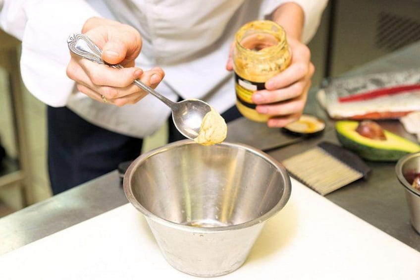 A person preparing food, stirring a mixture in a metal bowl, with a jar and a spoon visible. 2