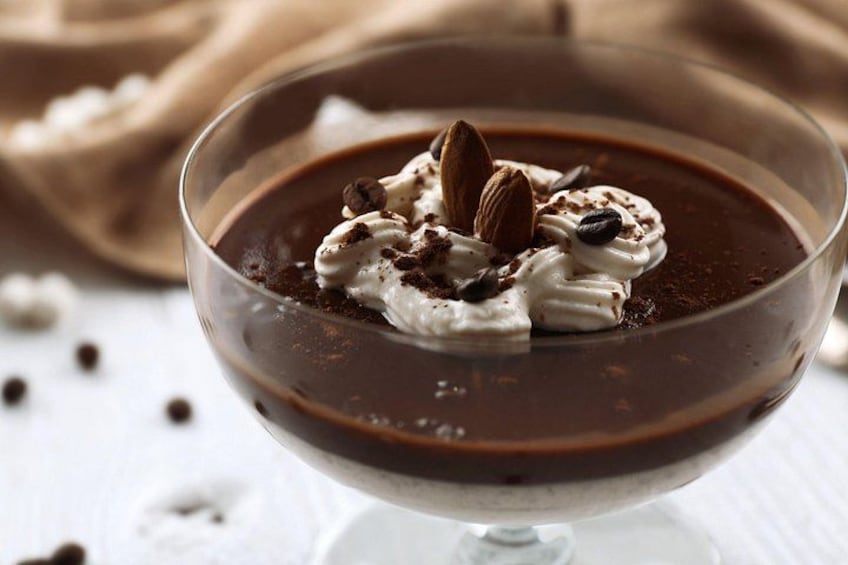 A dessert in a glass bowl with whipped cream, almonds, and chocolate shavings. 3