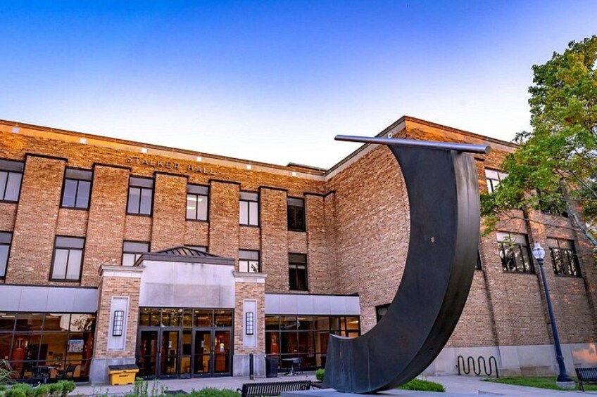 A brick building with a large curved metal sculpture in front. 2