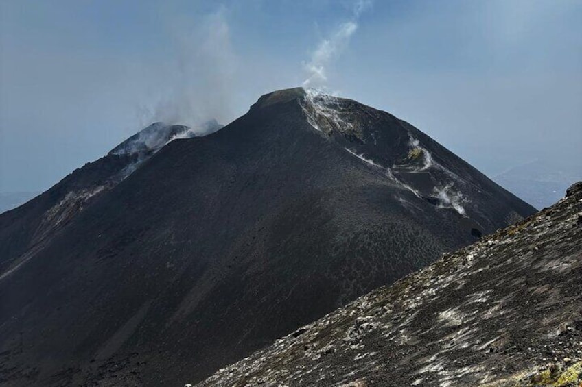 A mountain with a visible smoke plume, rocky terrain, and a clear sky. 1