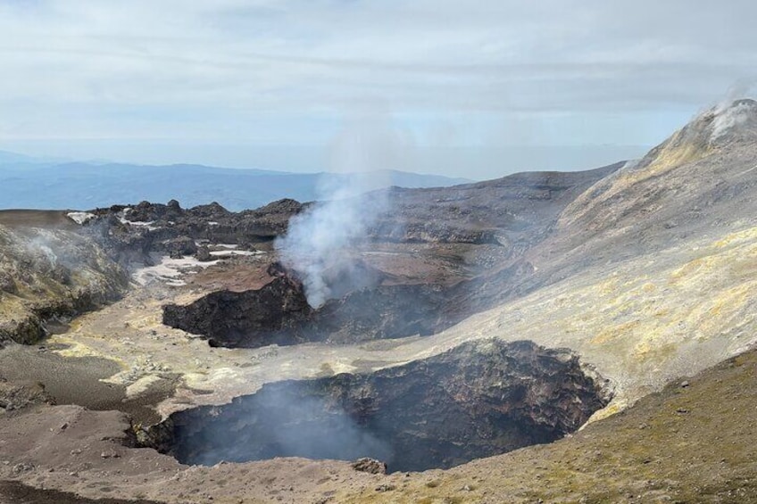 A volcanic landscape with steam vents and a crater. 2