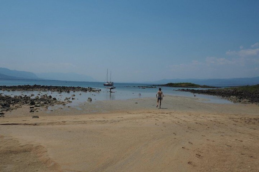 A beach with a person walking, a boat in the water, and distant mountains. 5
