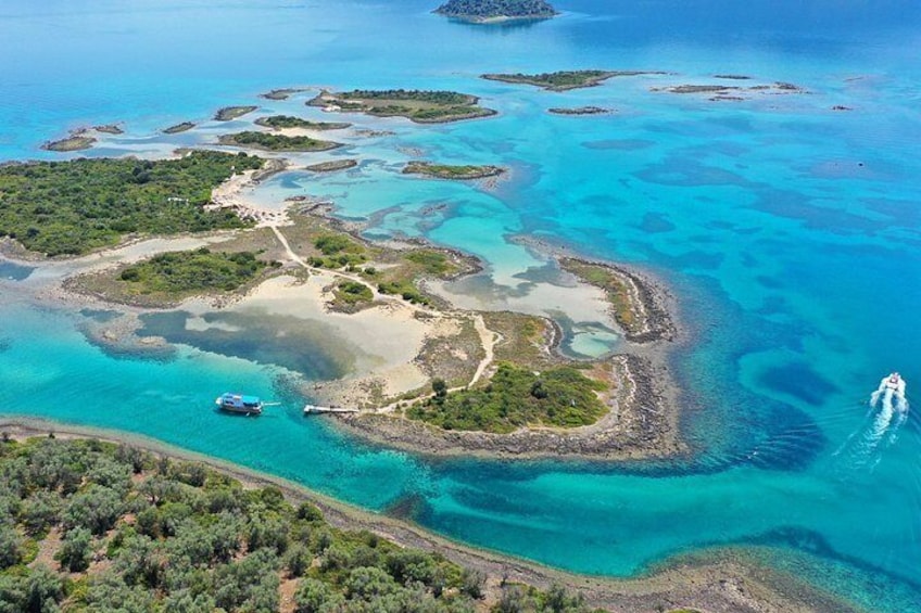 An aerial view of a turquoise lagoon with small islands, a boat, and a wake trail. 2