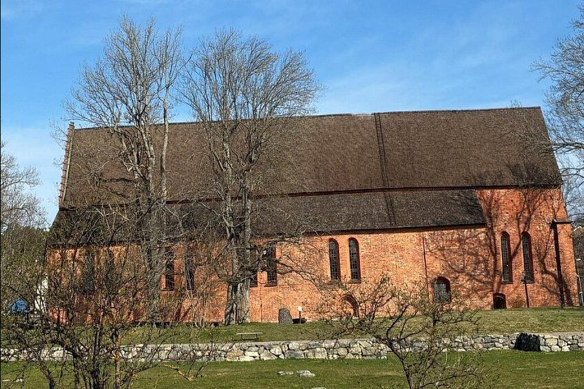 En stor murstensbygning med skråt tag, omgivet af træer og en stenvæg. 2