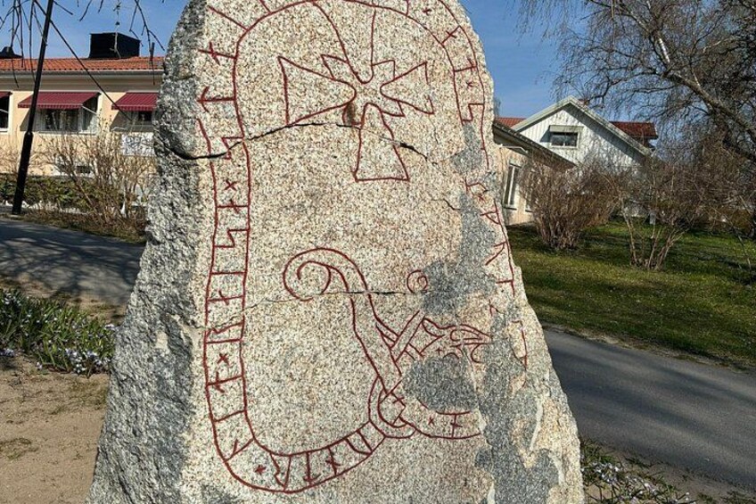 En stor sten med røde markeringer, en vej og huse i baggrunden. 5