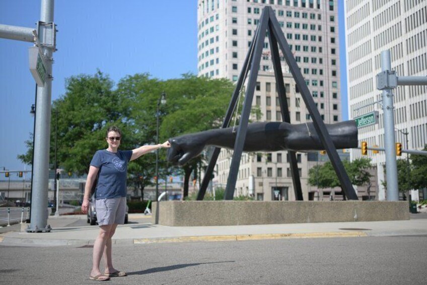 A person standing in front of a sculpture with a cityscape in the background. 5