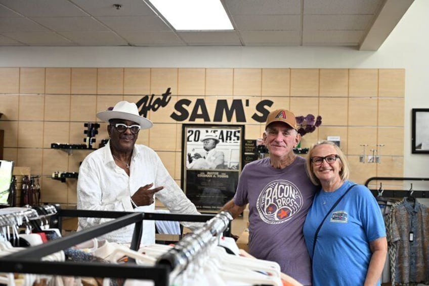 Three people in a store with a sign that reads 'SAM'S' and a poster of a car. 3