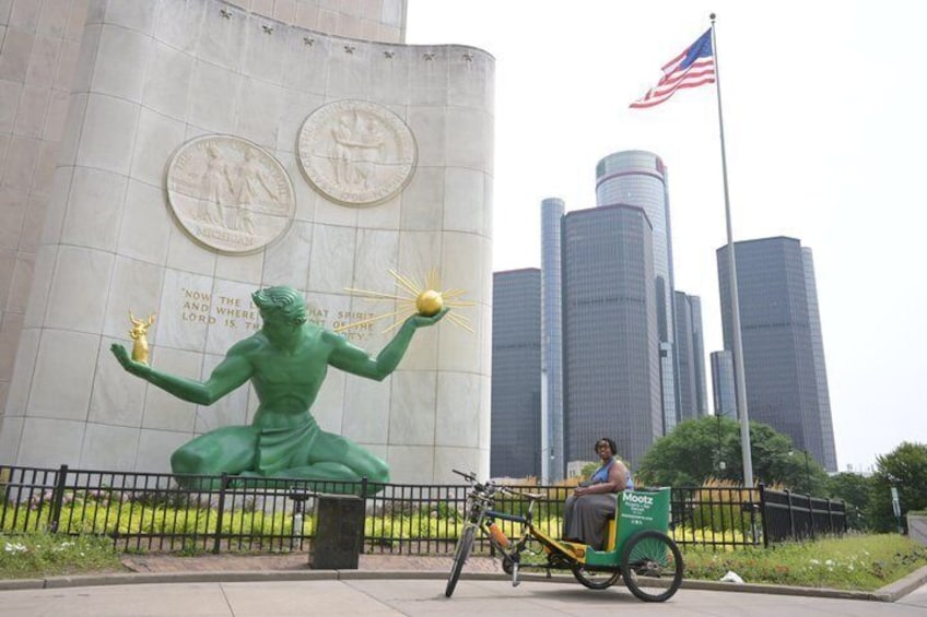 A large green statue of a figure with multiple arms, a person riding a bicycle, and tall buildings in the background. 1