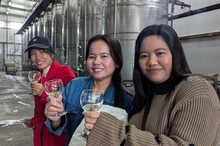 Three people holding wine glasses in a large industrial building with metal tanks. 4