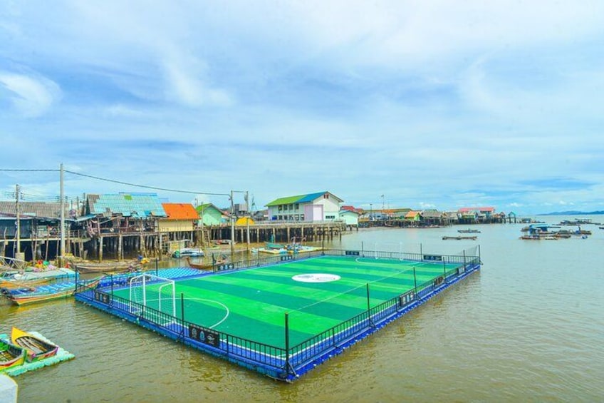 A floating sports court surrounded by water, with buildings and boats in the background. 2
