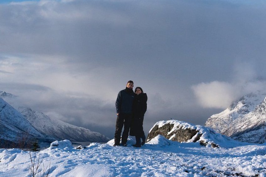 Una pareja de pie sobre una montaña nevada con afloramientos rocosos y un cielo nublado. 4