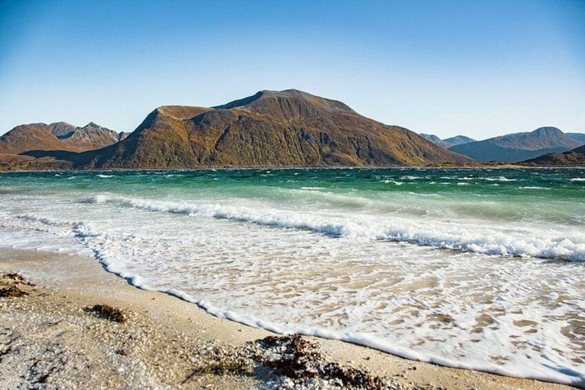 A beach with waves, rocky shore, and mountains in the background. 2