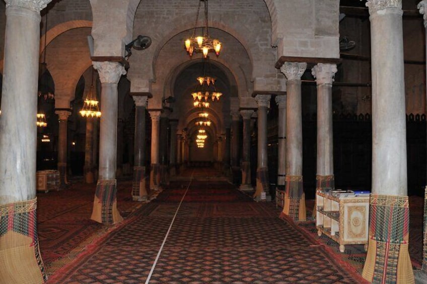 A long corridor with arches, columns, and patterned carpets. 1