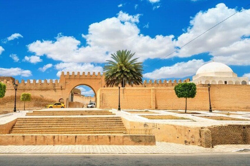 A historical gate with a dome in the background, a palm tree, and a yellow car. 2