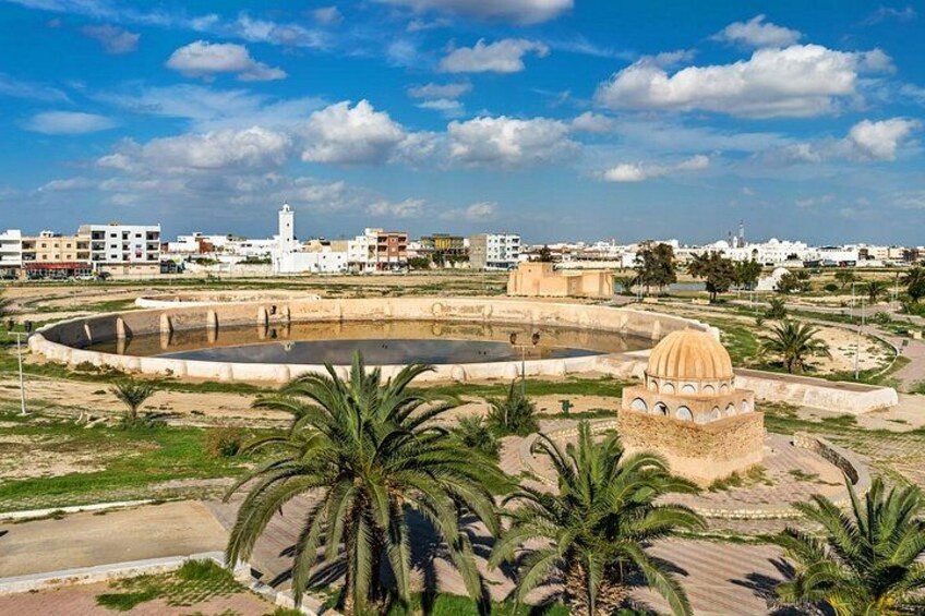 Un paisaje urbano costero con una gran fuente circular, palmeras y un edificio de forma distintiva en forma de cúpula. 3