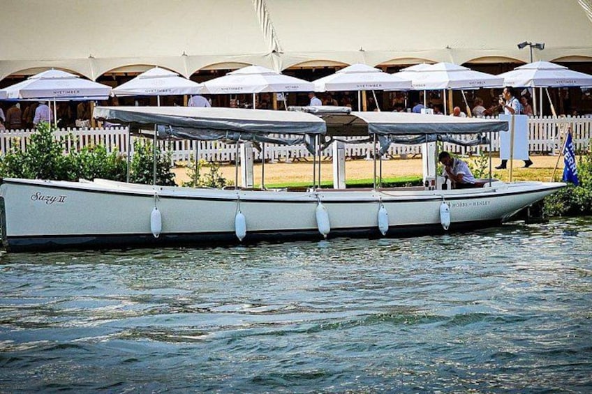 Un bateau à rames, baptisé « Sazy II », était amarré près d’une promenade en bord de mer, avec des parasols et une clôture blanche en bois en arrière-plan. 4