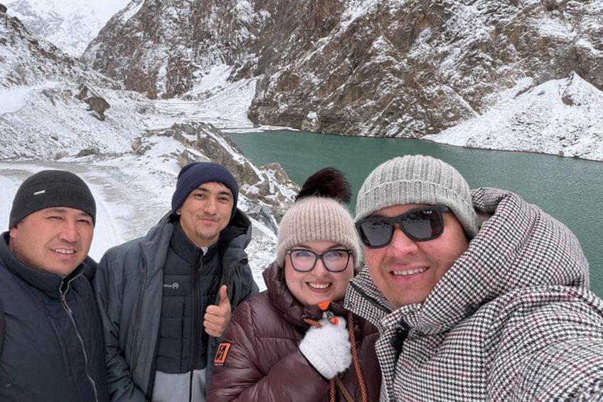 A group of people standing by a snow-covered lake with mountains in the background. 1