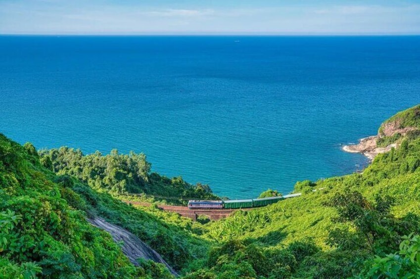 Ett tåg på en kustnära järnvägssträcka, omgivet av frodig grönska och havet. 4
