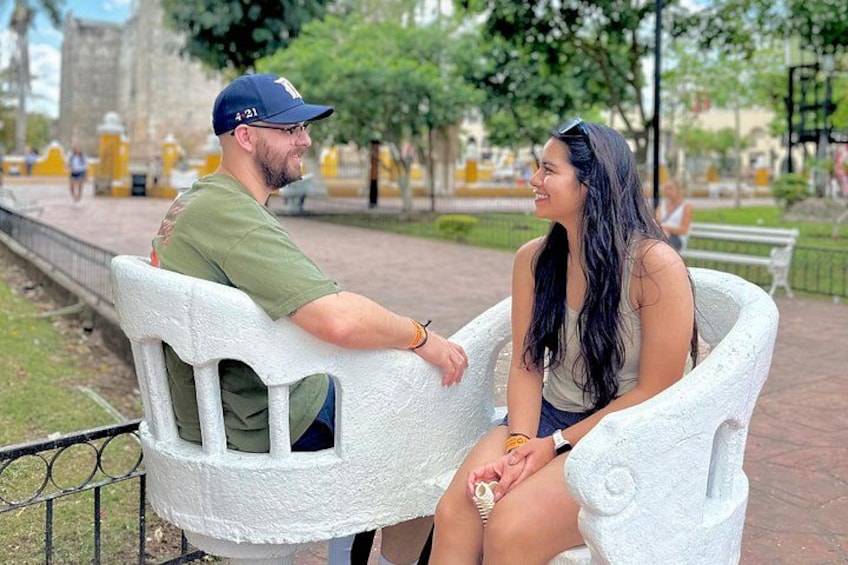 Two people sitting on a white bench in a park with a stone building in the background. 3