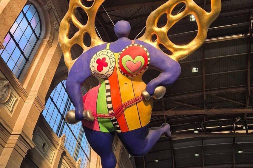 A colorful, abstract sculpture with a heart and a flower design, set against a building with large windows and a metal ceiling. 2
