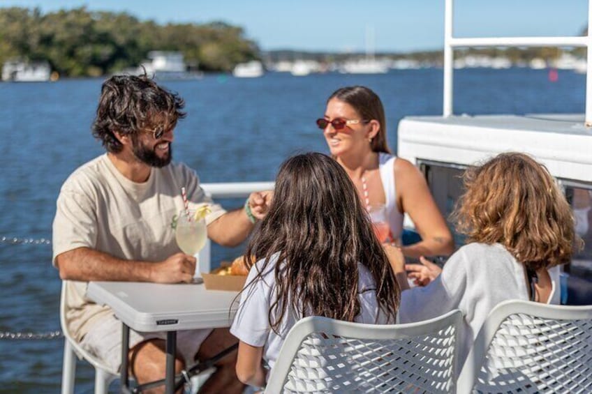 A group of people sitting at a table on a boat, enjoying drinks and food. 2