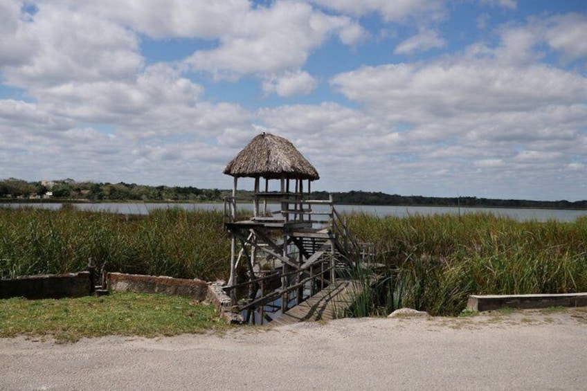 A thatched-roof structure by a lake with a clear sky. 4