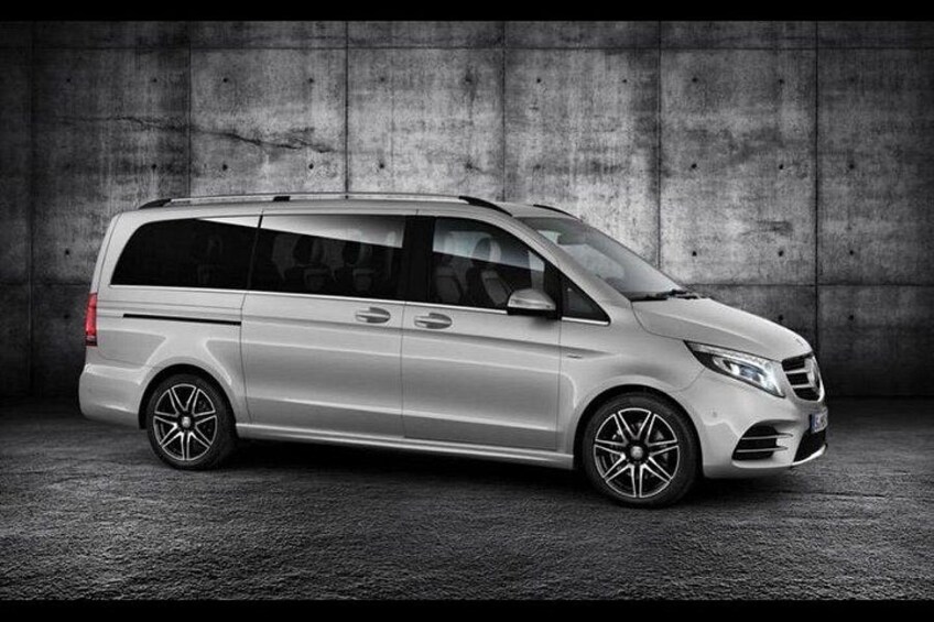 A silver minivan parked in front of a concrete wall. 5