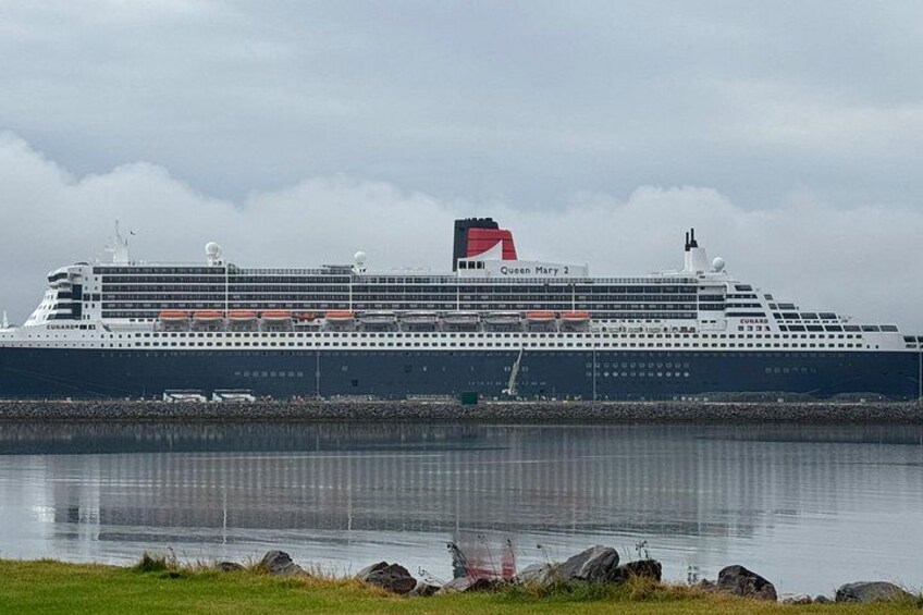 A large cruise ship named Queen Mary 2 docked at a port with calm waters and a cloudy sky. 4