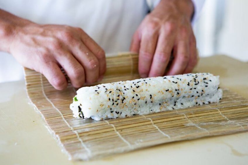 A person rolling sushi on a bamboo mat. 2