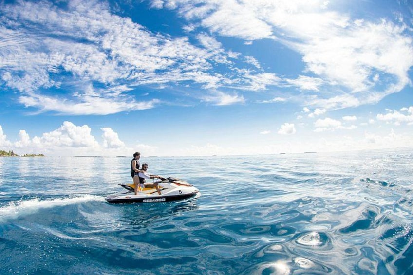 Iemand scheert met een jetski over kalm water op een heldere dag, met een kustlijn in de verte. 2