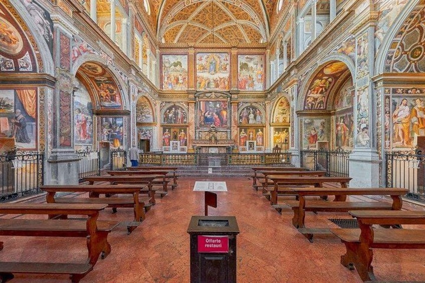 Interno di una chiesa con file di bancali, un altare centrale e affreschi dettagliati sulle pareti. 2