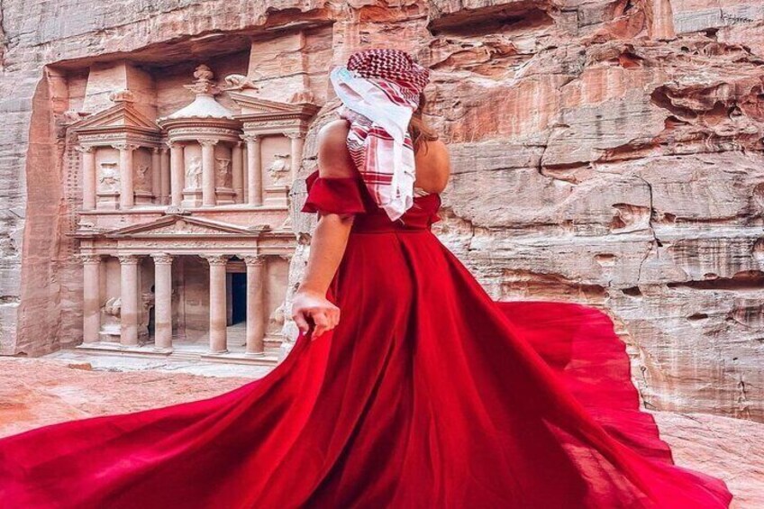 A person in a red dress standing in front of a carved rock facade. 1