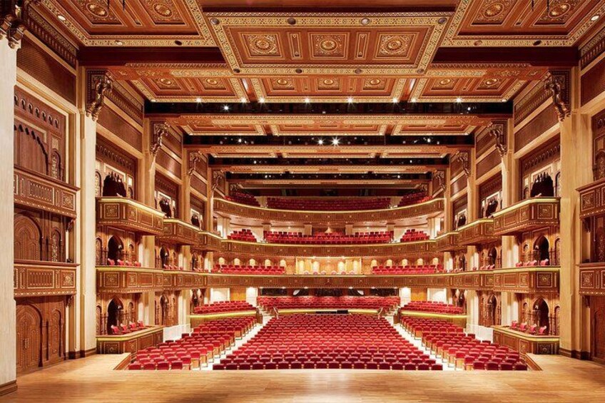 A grand auditorium with ornate wood paneling, red seating, and a central stage. 3