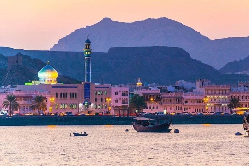 A mosque with a dome and minaret, a body of water with boats, and mountains in the background. 2