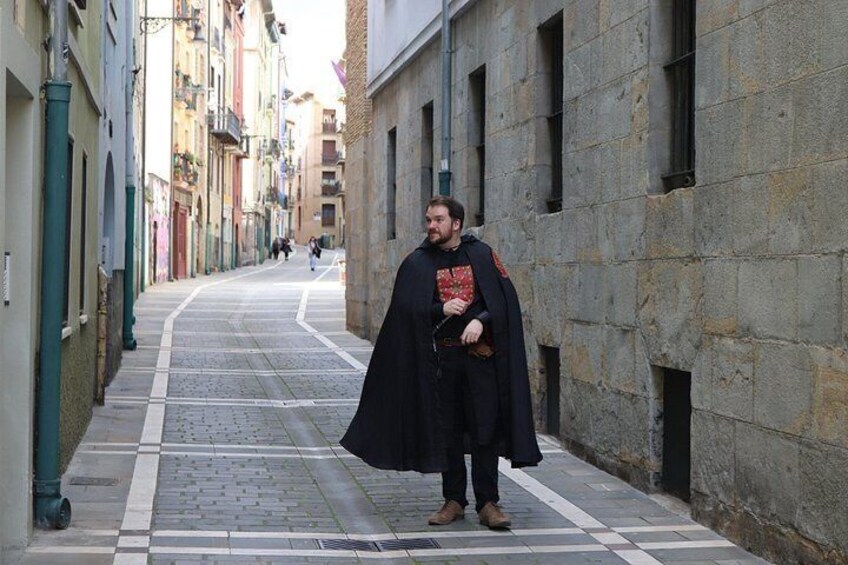 A person in medieval costume standing on a cobblestone street with buildings on either side. 4