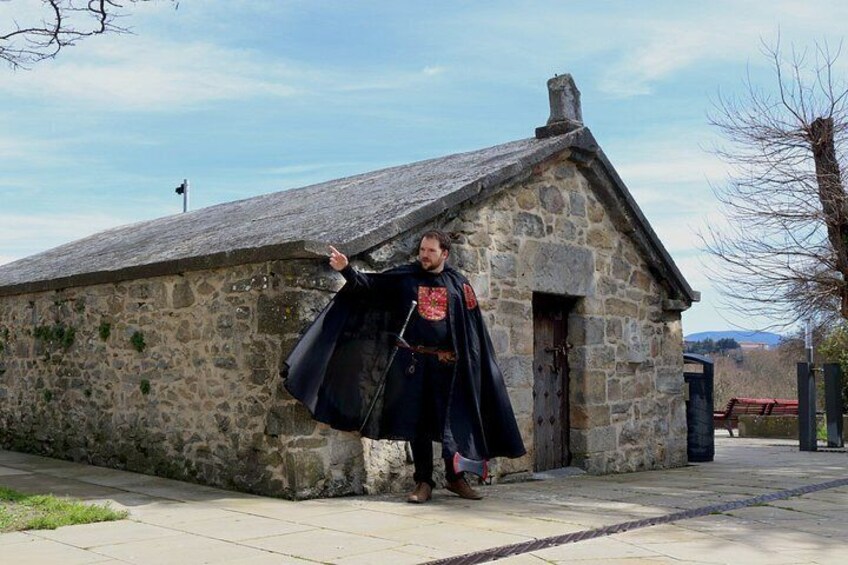 A person in medieval costume standing in front of a stone building with a pointed roof. 2