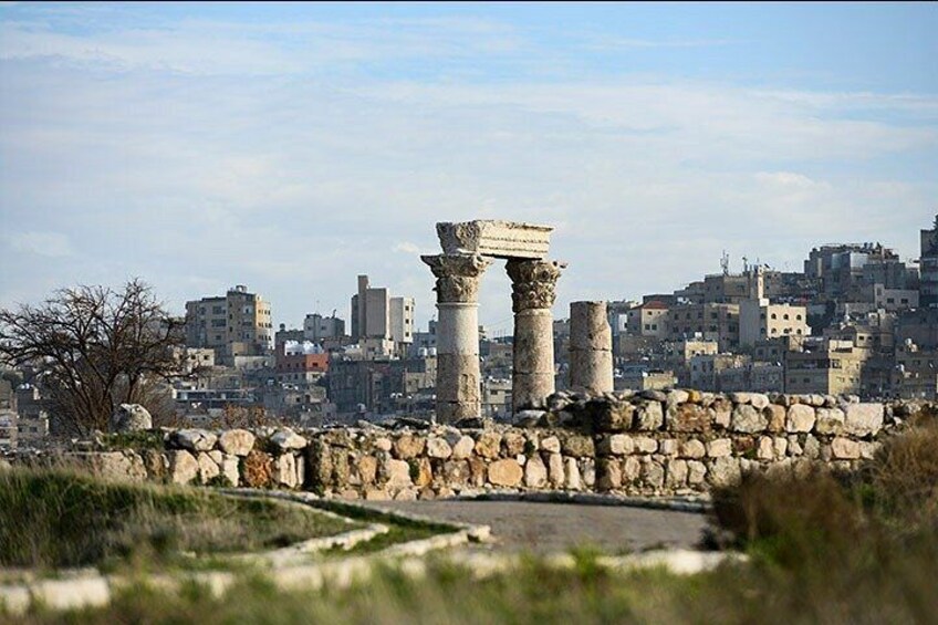 Ancient ruins with columns, a stone wall, and a cityscape in the background. 3