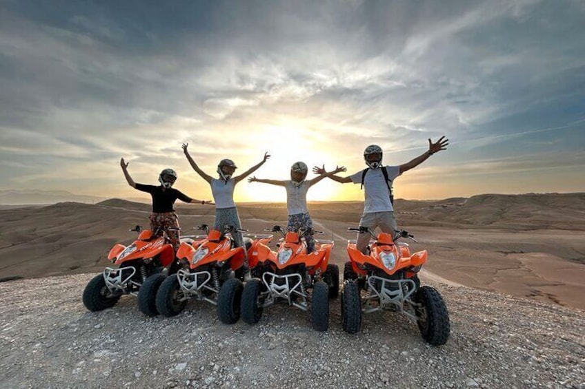 Four people on quad bikes in a desert landscape with a sunset in the background. 1