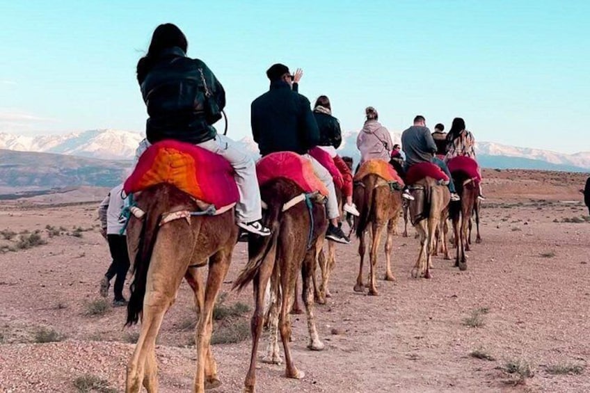 A group of people riding camels in a desert landscape with mountains in the background. 5