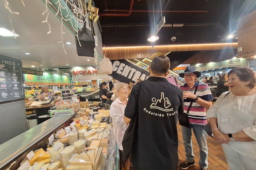 A cheese display in a market with people browsing. 5