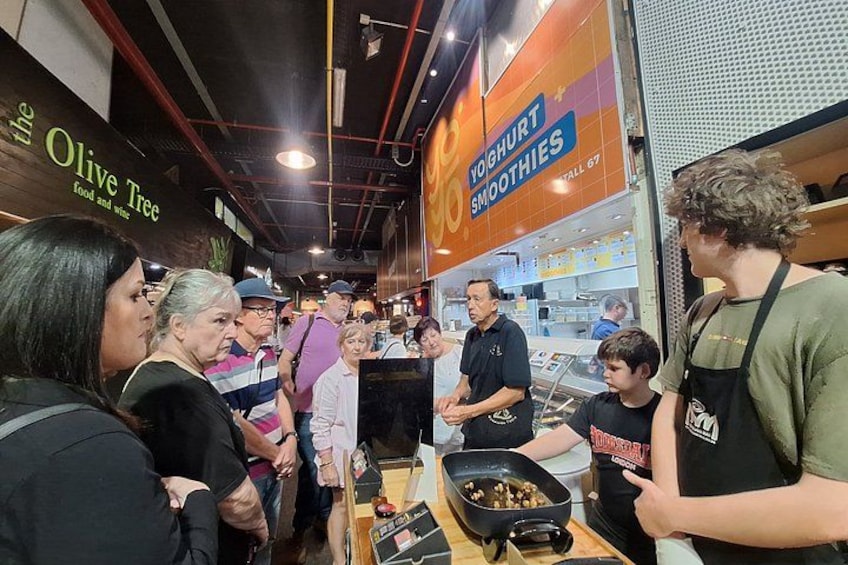 A busy food stall with a sign for 'Yoghurt Smoothies' and another for 'Olive Tree'. 2