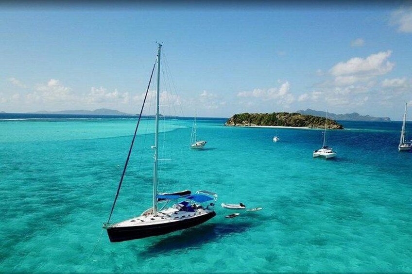 A turquoise sea with sailboats anchored near a small island. 2