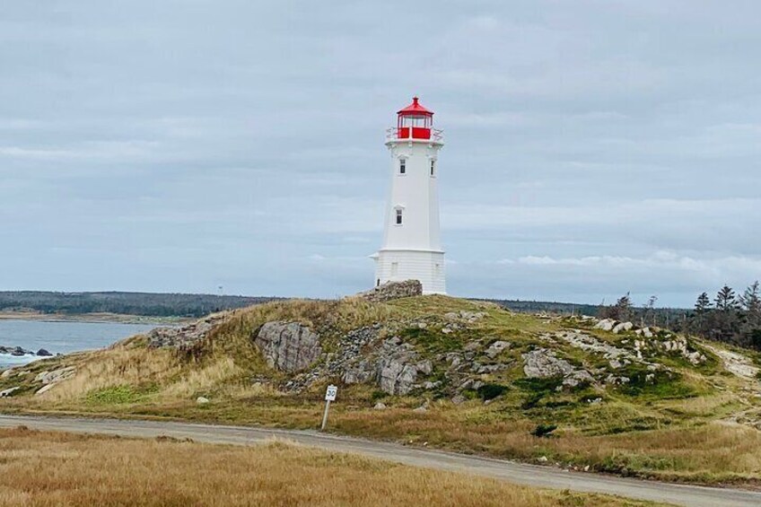 A white lighthouse with a red top on a grassy hill by the coast. 5