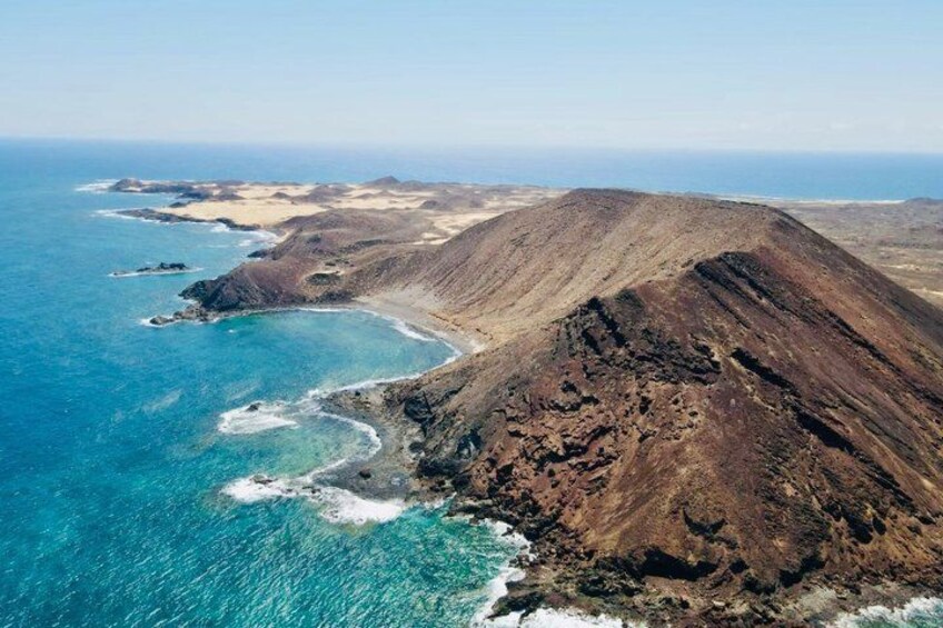 A coastal landscape with a prominent hill, clear blue waters, and a sandy beach. 2