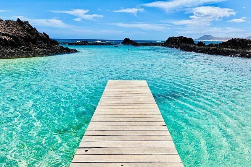A wooden pier extending into clear turquoise water, surrounded by rocky formations. 1