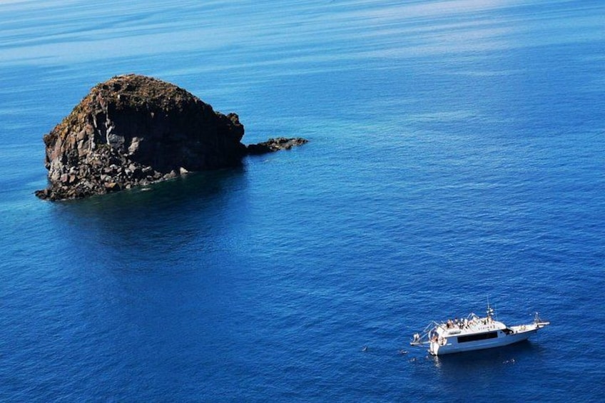 A rocky island surrounded by calm blue waters with a boat anchored nearby. 1