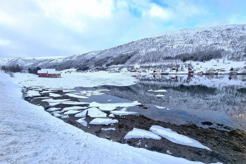 A snowy landscape with a river, ice floes, a red building, and snow-covered hills. 3